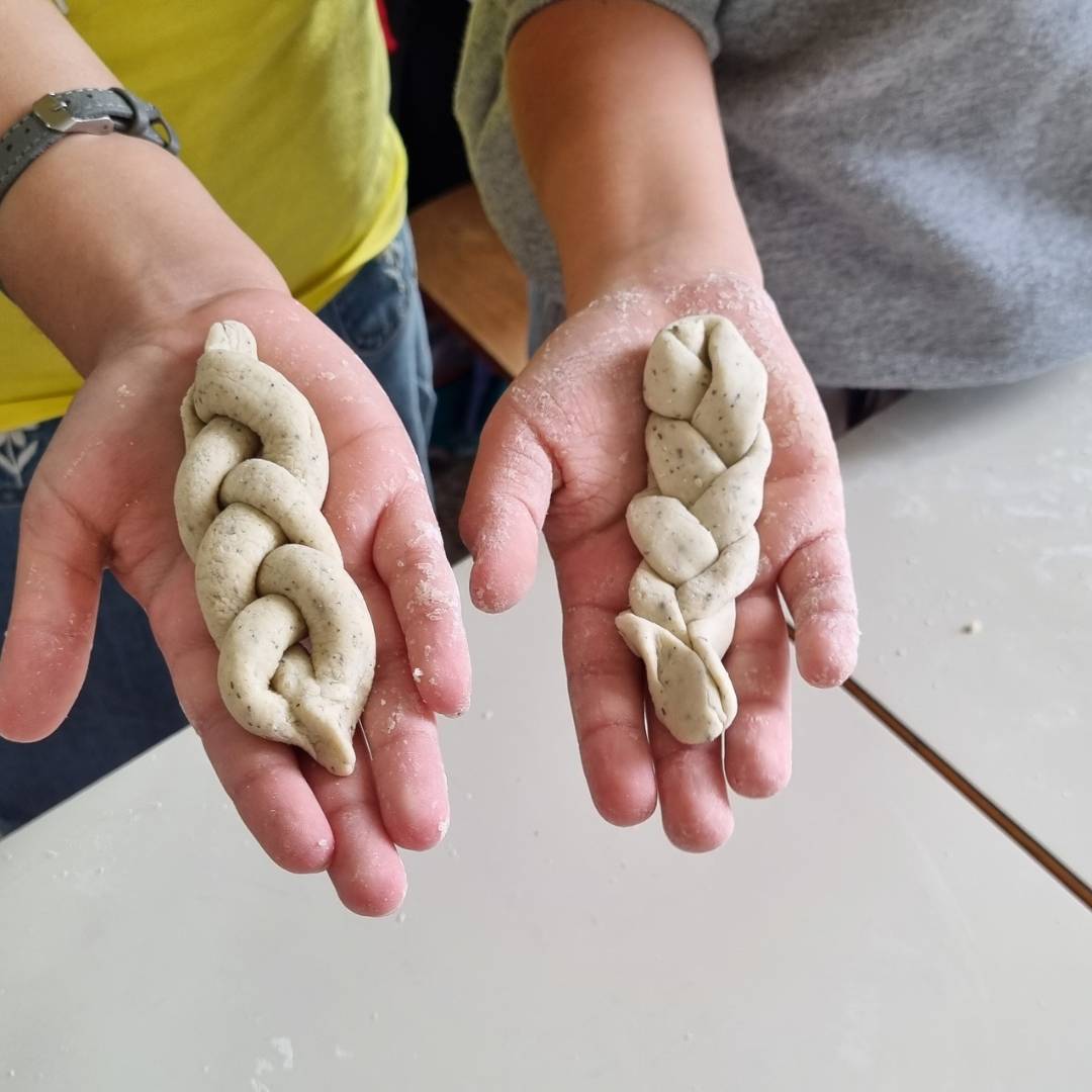 Mani di giovani che mostrano forme di impasto intrecciate durante i laboratori esperienziali a Novara incentrati sulla metafora del pane per l'espressione emotiva.