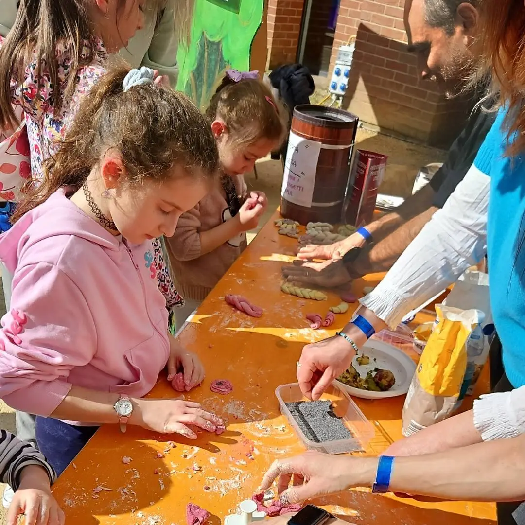 Bambine e adulti partecipano all'aperto a un'attività pratica e manipolativa intorno a un tavolo, durante i laboratori esperienziali a Novara incentrati sullo sviluppo dell'intelligenza emotiva e psicofisica.